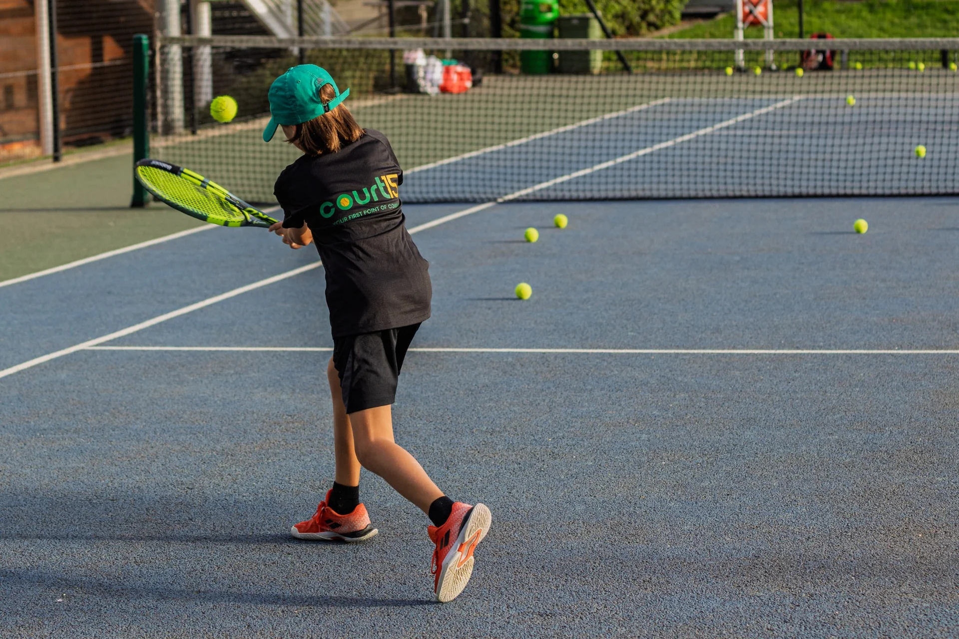 Junior tennis player wearing a Court15 shirt hitting a backhand on an outdoor court