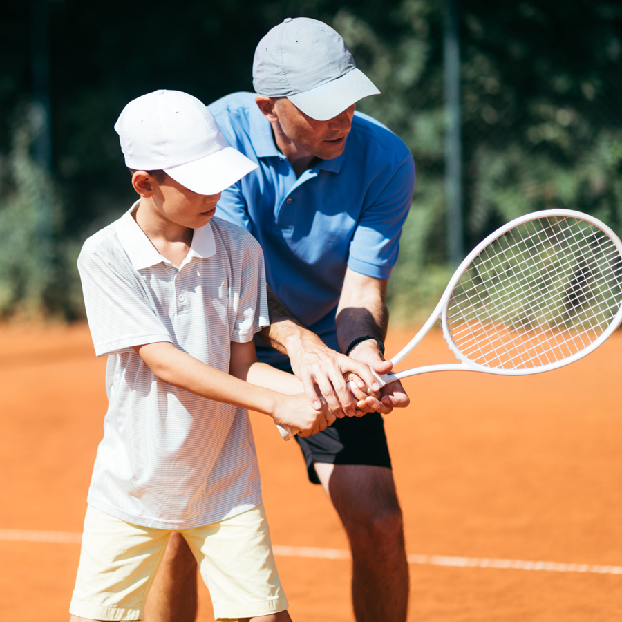 Tennis coach helping a young player practise their racket technique on court
